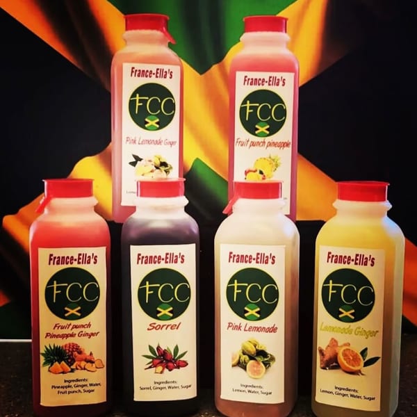 Six bottles of France-Ella's beverages, including sorrel and lemonade, against a Jamaican flag.