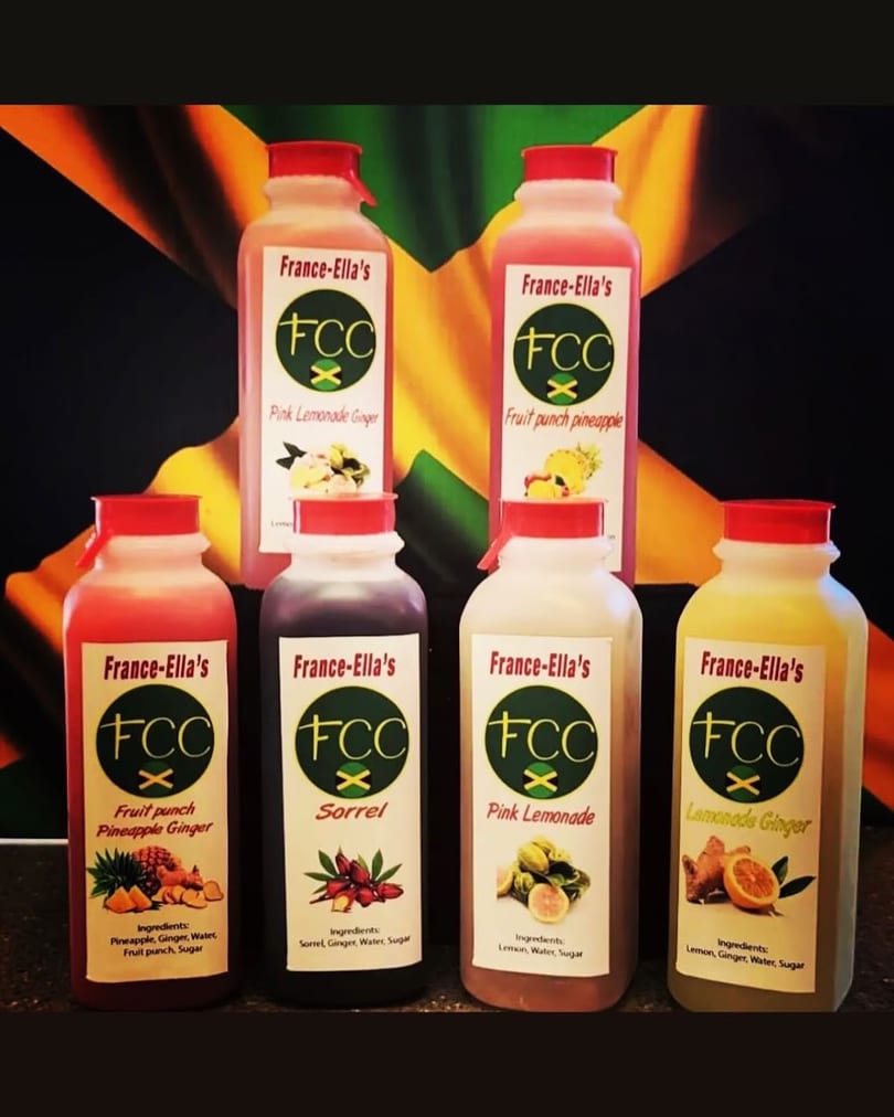Six bottles of France-Ella's beverages, including sorrel and lemonade, against a Jamaican flag.