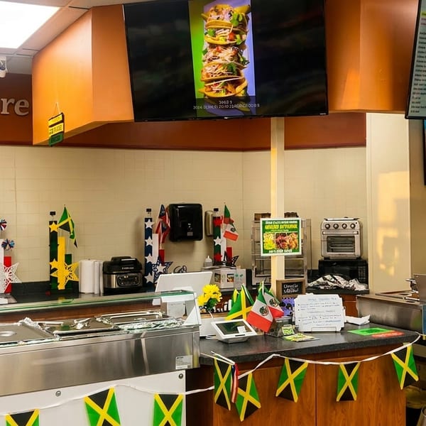 A Quick Eats Grille counter with food warmers, digital menus, and international flag decorations.