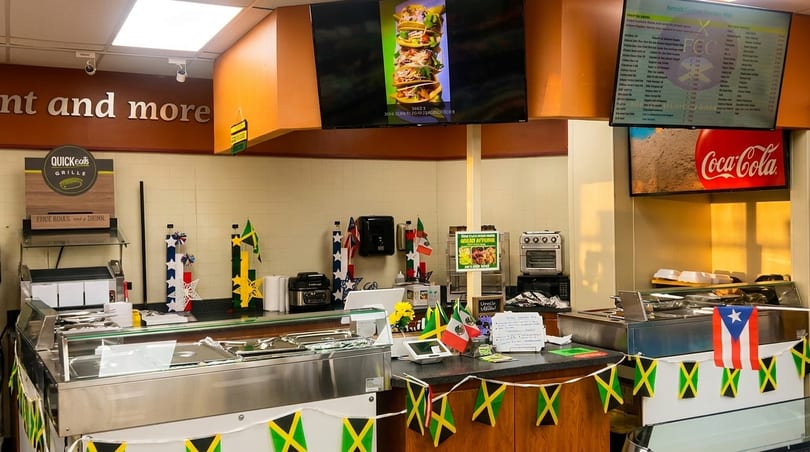 A Quick Eats Grille counter with food warmers, digital menus, and international flag decorations.